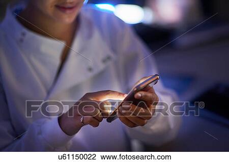 Stock Image - Scientist in laboratory texting on smartphone. Fotosearch