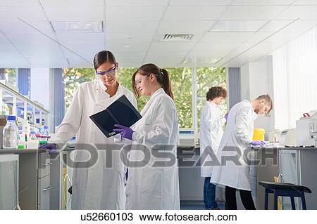 Stock Image - Scientists in laboratory discussing notebook. Fotosearch