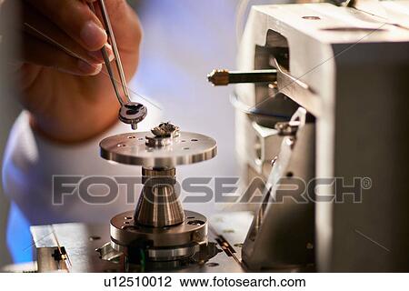 Stock Image - Scientists placing object on scientific equipment using tweezers. Fotosearch