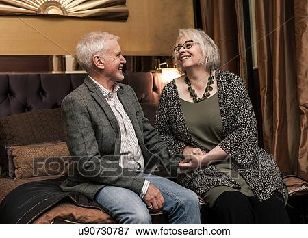 Stock Photo - Senior couple smiling and chatting on bed. Fotosearch