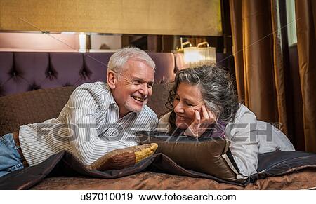 Senior couple smiling and chatting on bed View Large Photo Image Stock Photo - Senior couple smiling and chatting on bed. Fotosearch
