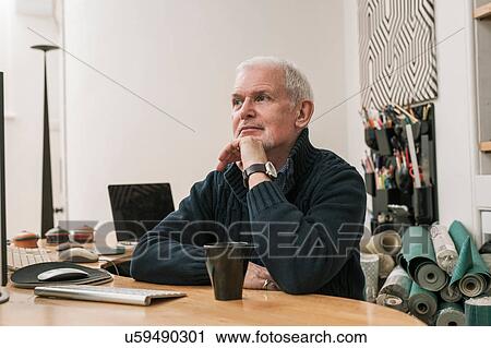 Stock Image - Senior man daydreaming at work desk. Fotosearch