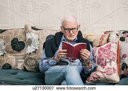 Stock Photo - Senior man reading book on couch. Fotosearch