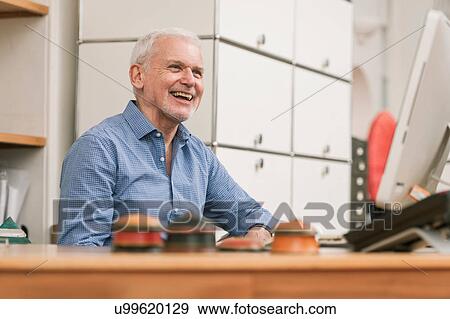 Stock Photo - Senior man smiling at work desk. Fotosearch
