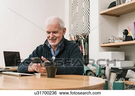 Senior man smiling, using mobile phone at work desk View Large Photo Image Stock Photograph - Senior man smiling, using mobile phone at work desk. Fotosearch