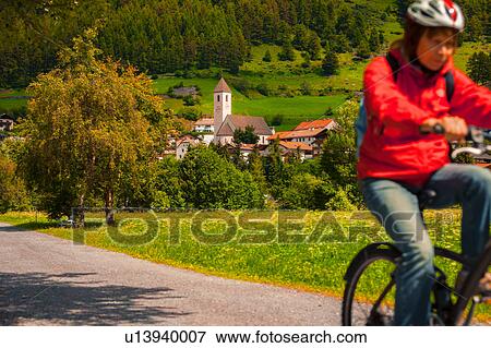 Stock Photo - Senior woman cycling along village path in Vinschgau Valley, South Tyrol, Italy. Fotosearch