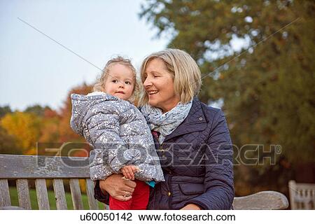 Stock Image - Senior woman sitting with toddler granddaughter in autumn park. Fotosearch