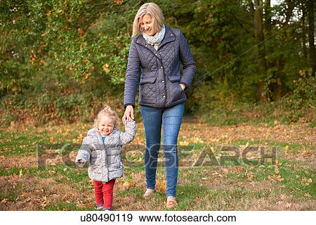 Stock Photo - Senior woman strolling with toddler granddaughter in autumn park. Fotosearch