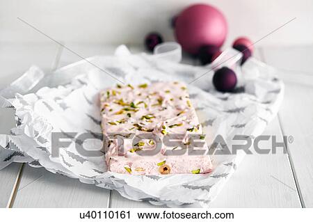 Stock Image - Slice of pistachio and rose nougat with Christmas baubles. Fotosearch