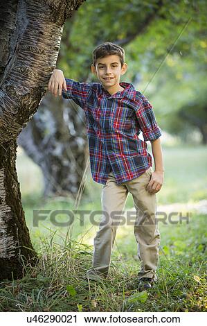 Stock Image - Smiling boy standing by cherry tree. Fotosearch