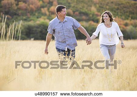 Smiling couple holding hands while walking in field View Large Photo Image Stock Photo - Smiling couple holding hands while walking in field. Fotosearch
