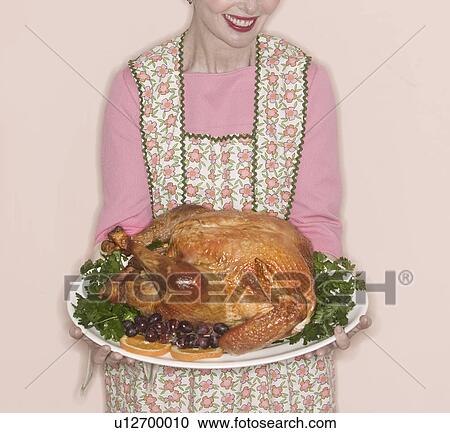Stock Image - Smiling senior woman holding garnished turkey on plate. Fotosearch