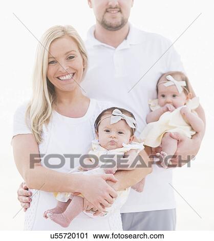 Stock Image - Studio shot portrait of happy family with two baby girls (2-5 months) on white background. Fotosearch