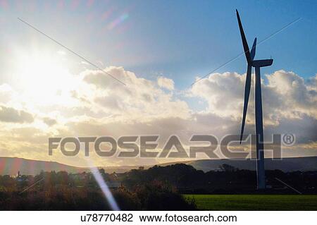 Stock Image - Sunlit silhouetted wind turbine in rural landscape. Fotosearch