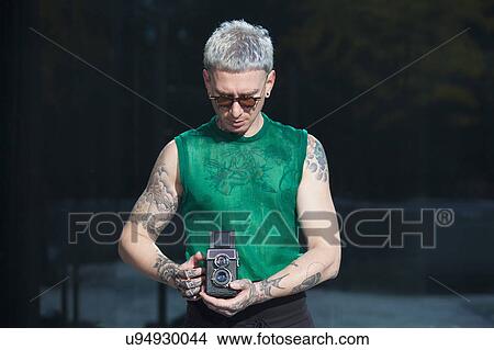Picture - Tattooed man holding vintage camera. Fotosearch