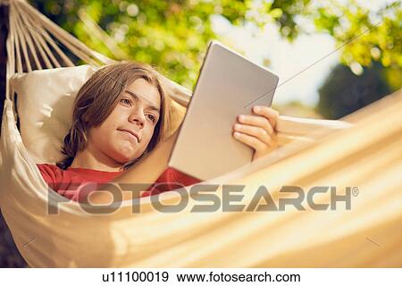 Teenage boy reclining in garden hammock using digital tablet touchscreen View Large Photo Image Stock Photo - Teenage boy reclining in garden hammock using digital tablet touchscreen. Fotosearch