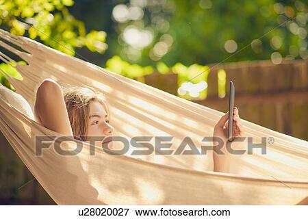 Stock Photo - Teenage boy reclining in garden hammock browsing digital tablet. Fotosearch