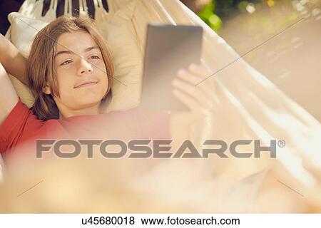 Teenage boy relaxing in garden hammock browsing digital tablet View Large Photo Image Stock Photo - Teenage boy relaxing in garden hammock browsing digital tablet. Fotosearch