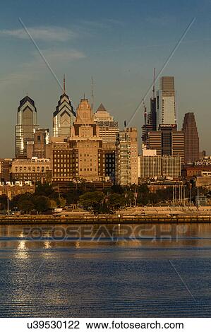 Stock Image - The skyscrapers of Philadelphia rise above the Delaware River at sunrise. Fotosearch