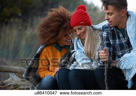 Stock Photo - Three adult friends sitting huddled together on beach at dusk. Fotosearch