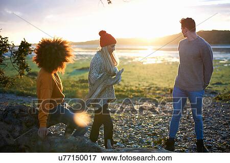 Three adult friends watching sunset over sea whilst collecting driftwood View Large Photo Image Stock Photo - Three adult friends watching sunset over sea whilst collecting driftwood. Fotosearch