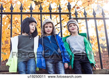 Stock Image - Three boys outdoors, leaning against fence, low angle view. Fotosearch
