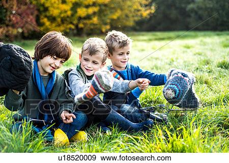 Stock Photo - Three boys, sitting together in field, in autumn. Fotosearch