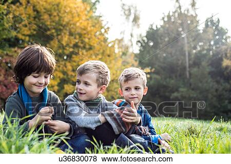 Stock Photo - Three boys, sitting together in field, in autumn. Fotosearch