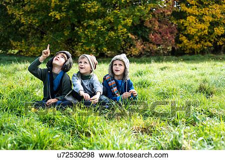Stock Photo - Three boys, sitting together in field, in autumn. Fotosearch