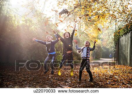 Stock Image - Three young boys, playing outdoors, throwing autumn leaves. Fotosearch