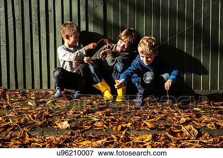 Three young boys, sitting against fence, surrounded by autumn leaves View Large Photo Image Stock Photo - Three young boys, sitting against fence, surrounded by autumn leaves. Fotosearch