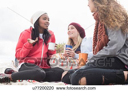 Stock Image - Three young women chatting on beach picnic, Western Cape, South Africa. Fotosearch