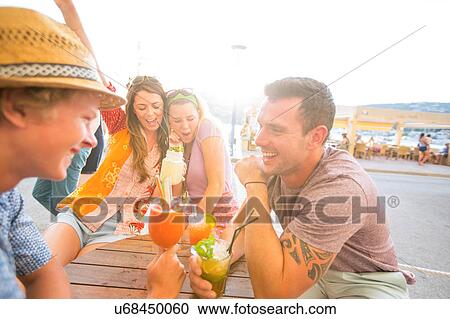 Stock Image - Two adult couples sharing cocktails at waterfront restaurant, Majorca, Spain. Fotosearch