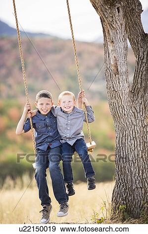 Stock Photo - Two boys (4-5, 6-7) sitting on swing. Fotosearch