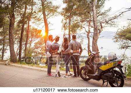 Stock Photo - Two couples with moped looking out at sunset from coastal road, Split, Dalmatia, Croatia. Fotosearch