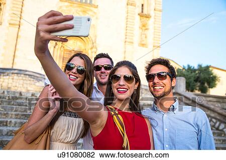 Stock Image - Two tourist couples in sunglasses taking selfie in front of church, Calvia, Majorca, Spain. Fotosearch