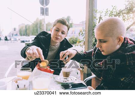 Stock Image - Two you female friends eating snack at sidewalk cafe. Fotosearch