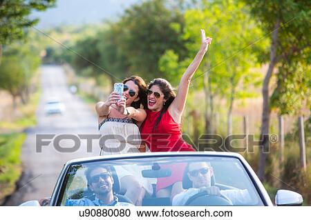 Stock Image - Two young female friends taking selfie whilst driving on rural road in convertible, Majorca, Spain. Fotosearch