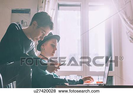 Two young female friends using smartphone and laptop in living room View Large Photo Image Stock Photo - Two young female friends using smartphone and laptop in living room. Fotosearch