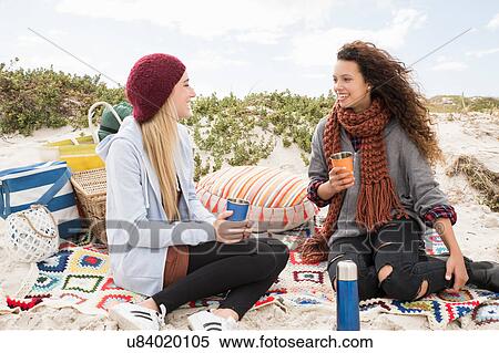 Stock Photography - Two young women chatting beach picnic, Western Cape, South Africa. Fotosearch