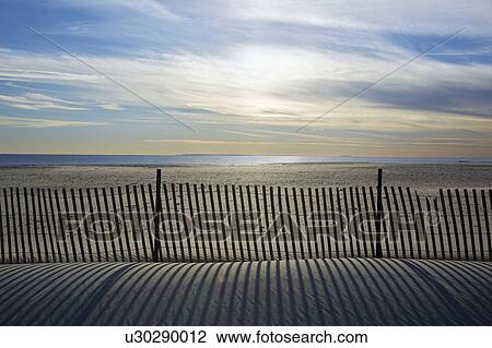 Stock Image - USA, New York, Lond Island, Fence by beach at sunset. Fotosearch