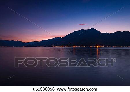 Stock Photograph - View of silhouetted mountains over Lake Como at night, Bellagio, Italy. Fotosearch