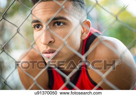 Stock Image - View through wire fence of young male athlete. Fotosearch
