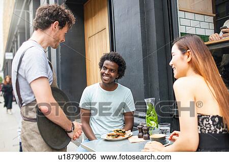 Stock Photograph - Waiter serving couple at city sidewalk cafe. Fotosearch