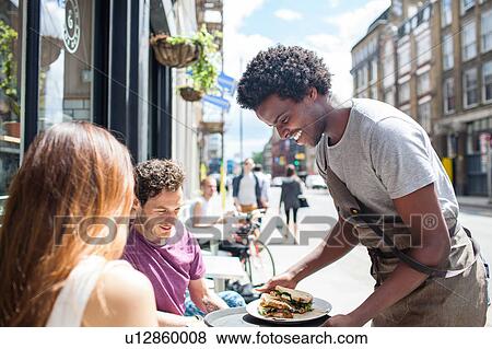 Waiter serving lunch to couple at city sidewalk cafe View Large Photo Image Stock Photo - Waiter serving lunch to couple at city sidewalk cafe. Fotosearch