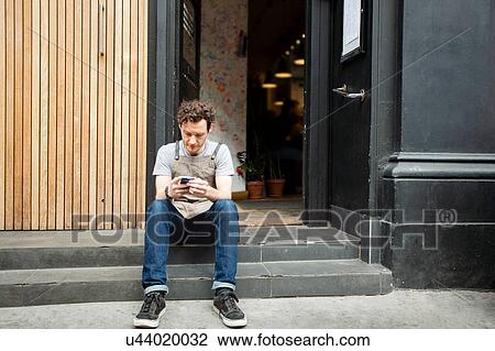 Waiter taking a break on cafe step looking at smartphone View Large Photo Image Stock Image - Waiter taking a break on cafe step looking at smartphone. Fotosearch