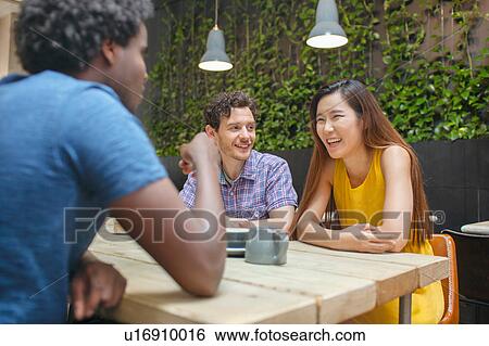 Stock Photograph - Woman and male friends chatting at coffee shop table. Fotosearch