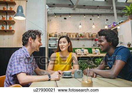 Stock Image - Woman and male friends chatting together in cafe. Fotosearch