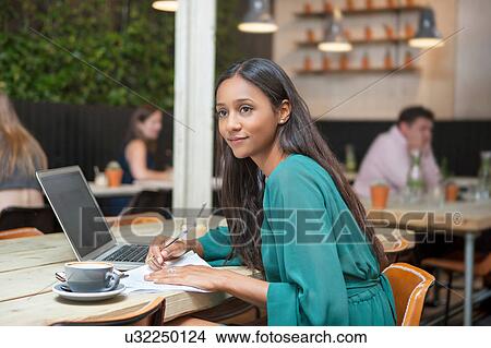 Picture - Woman gazing whilst doing paperwork at cafe table. Fotosearch