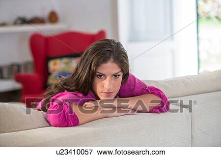 Stock Photo - Woman on sofa resting on elbows looking away. Fotosearch